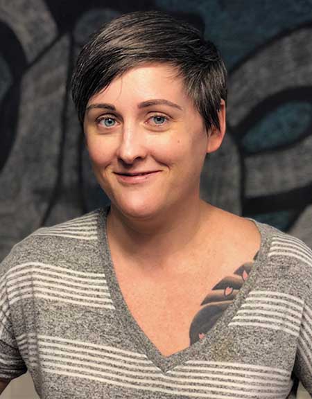 Portrait of smiling short-haired woman wearing a grey heather shirt with white horizontal stripes.